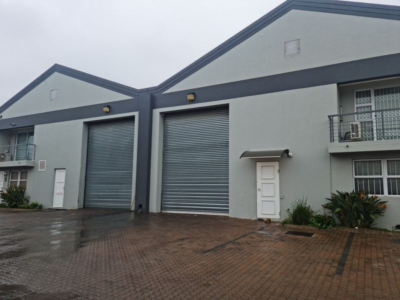 Front elevation of an industrial property featuring dual roller shutter doors, paved driveway access, and upper-level balcony access.