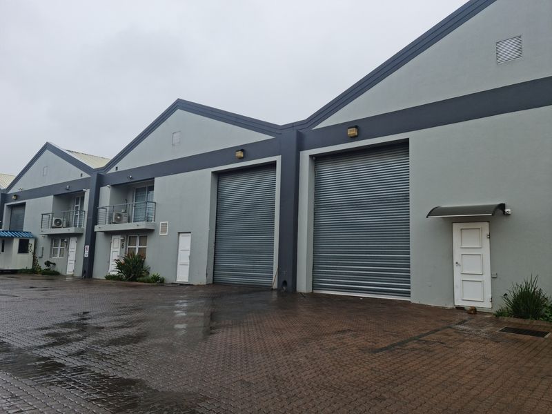 Exterior view of an industrial complex featuring multiple roller shutter doors, paved access area, and upper-level balconies.