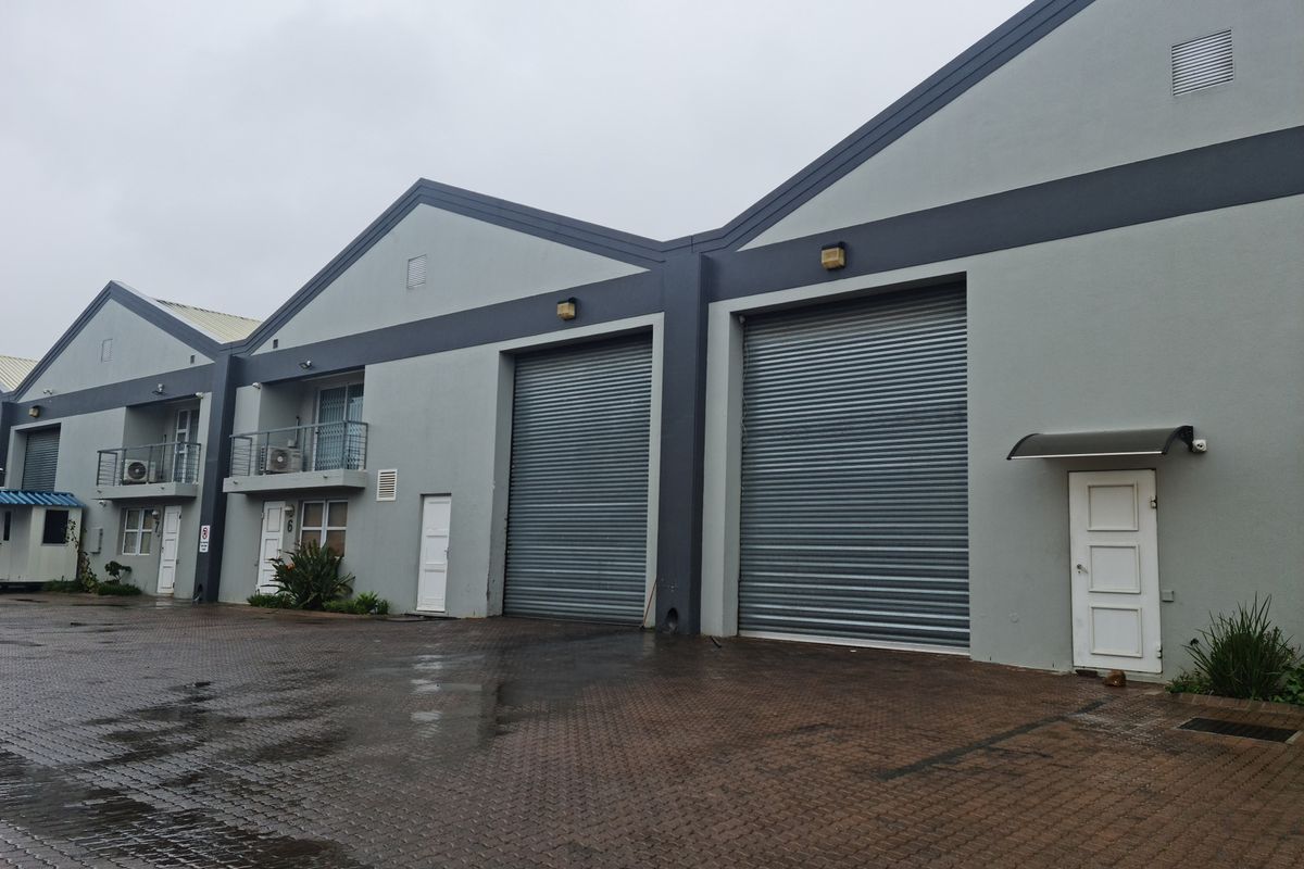Exterior view of an industrial complex featuring multiple roller shutter doors, paved access area, and upper-level balconies.