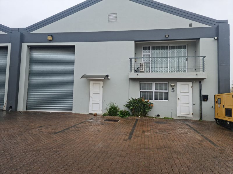 Front elevation of an industrial unit featuring a large roller shutter door, ground floor entrance, and an upper-level balcony with security gates.