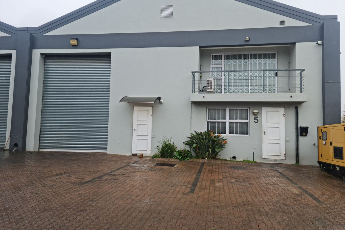 Front elevation of an industrial unit featuring a large roller shutter door, ground floor entrance, and an upper-level balcony with security gates.