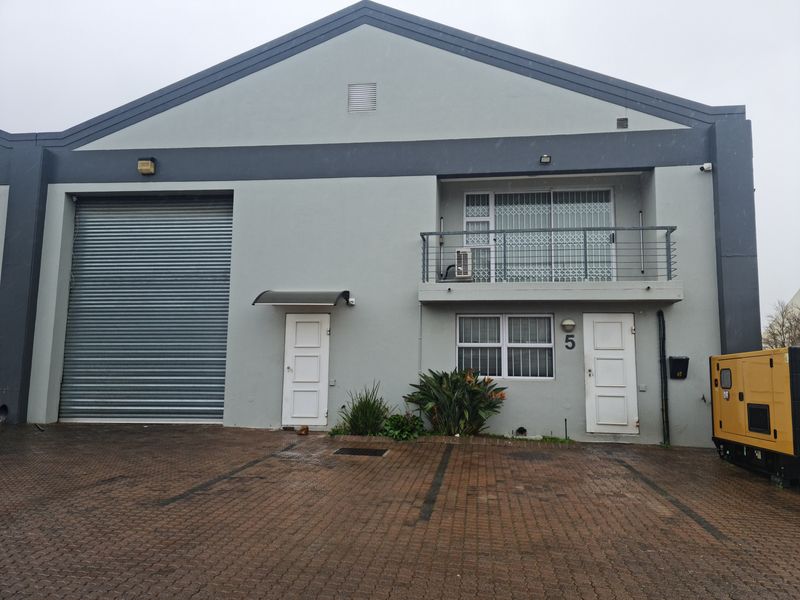 Front elevation of an industrial unit featuring a large roller shutter door, a private balcony, and dedicated paved parking space.