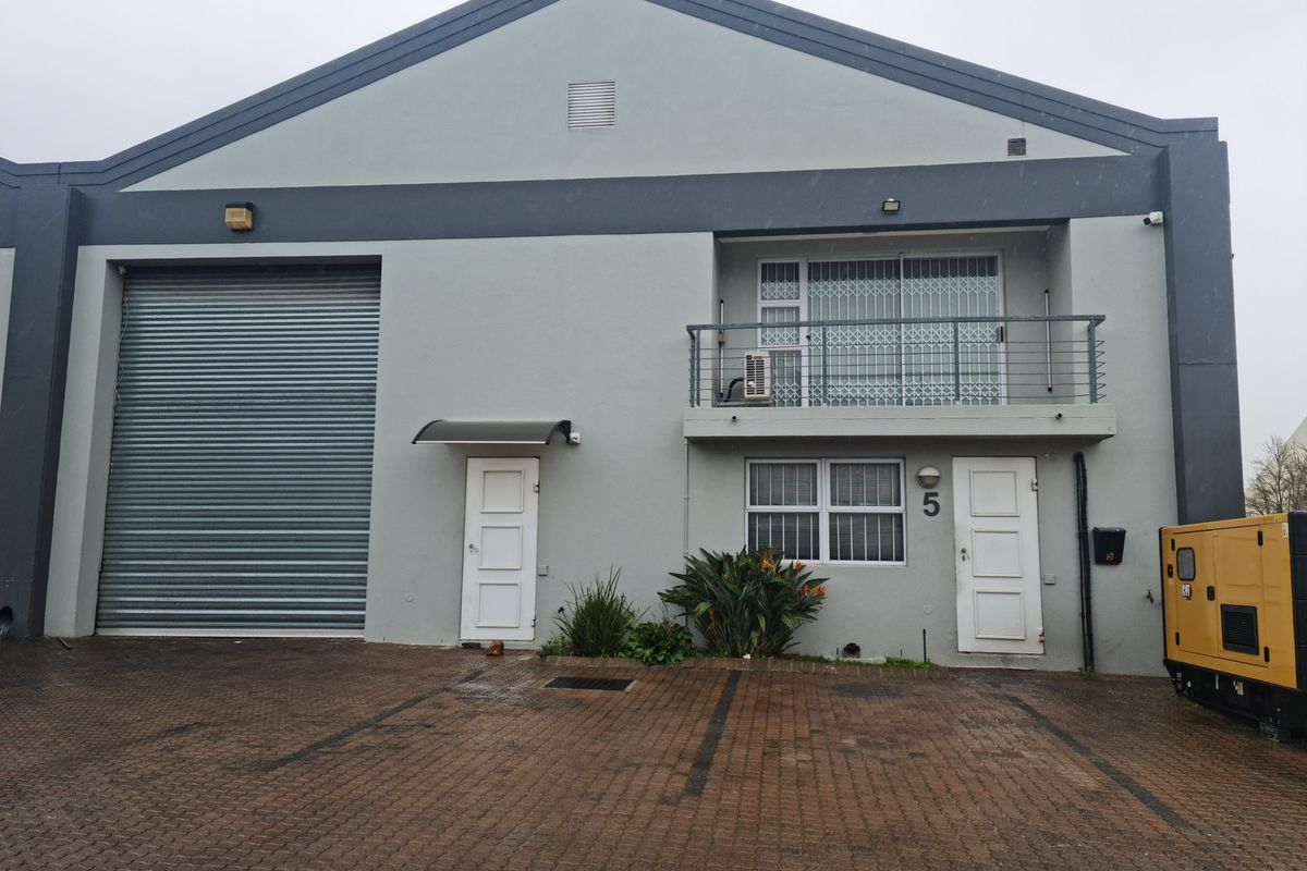 Front elevation of an industrial unit featuring a large roller shutter door, a private balcony, and dedicated paved parking space.