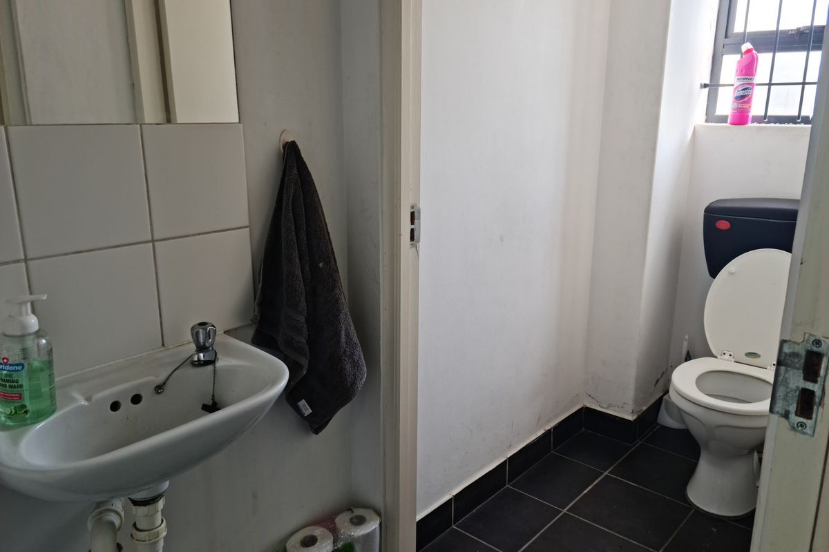 A functional industrial bathroom featuring a wall-mounted basin, tiled splashback, and a standard toilet suite with dark floor tiling.