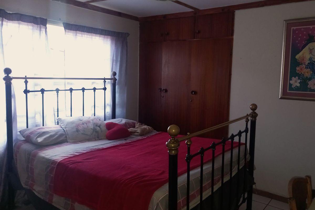 A bedroom featuring built-in wooden cupboards, tiled flooring, and a beamed ceiling, offering a functional space with classic architectural elements.
