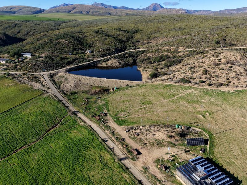 Aerial view of a farm property featuring a large dam, extensive agricultural land, and a solar energy installation on the main building roof.