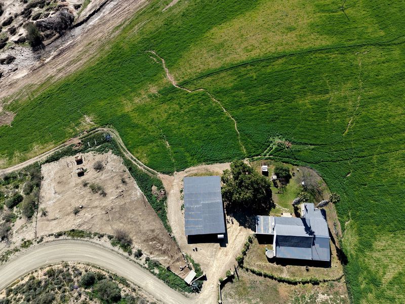 Aerial view of the farm property featuring main dwelling, outbuilding, gravel access road, and surrounding green agricultural land.