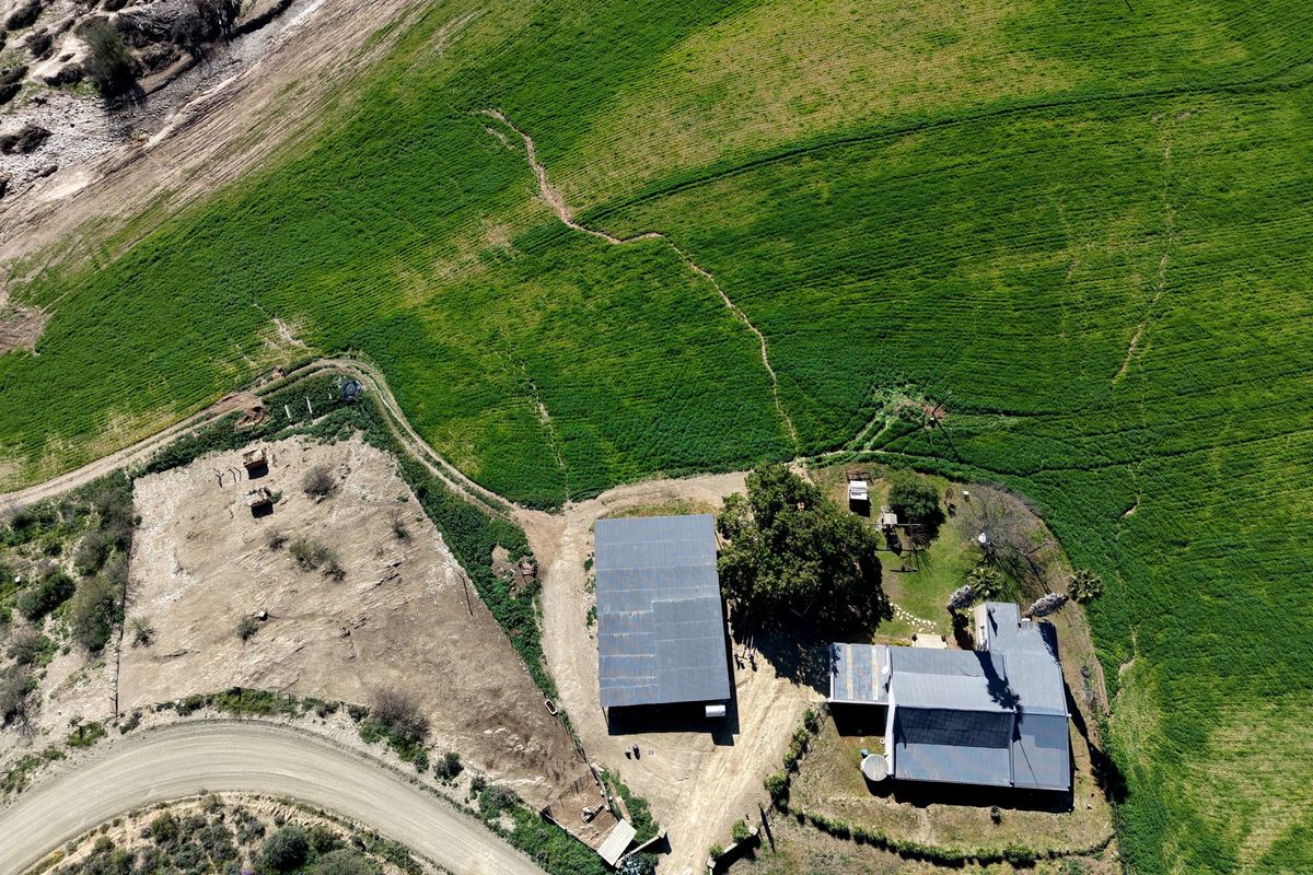 Aerial view of the farm property featuring main dwelling, outbuilding, gravel access road, and surrounding green agricultural land.