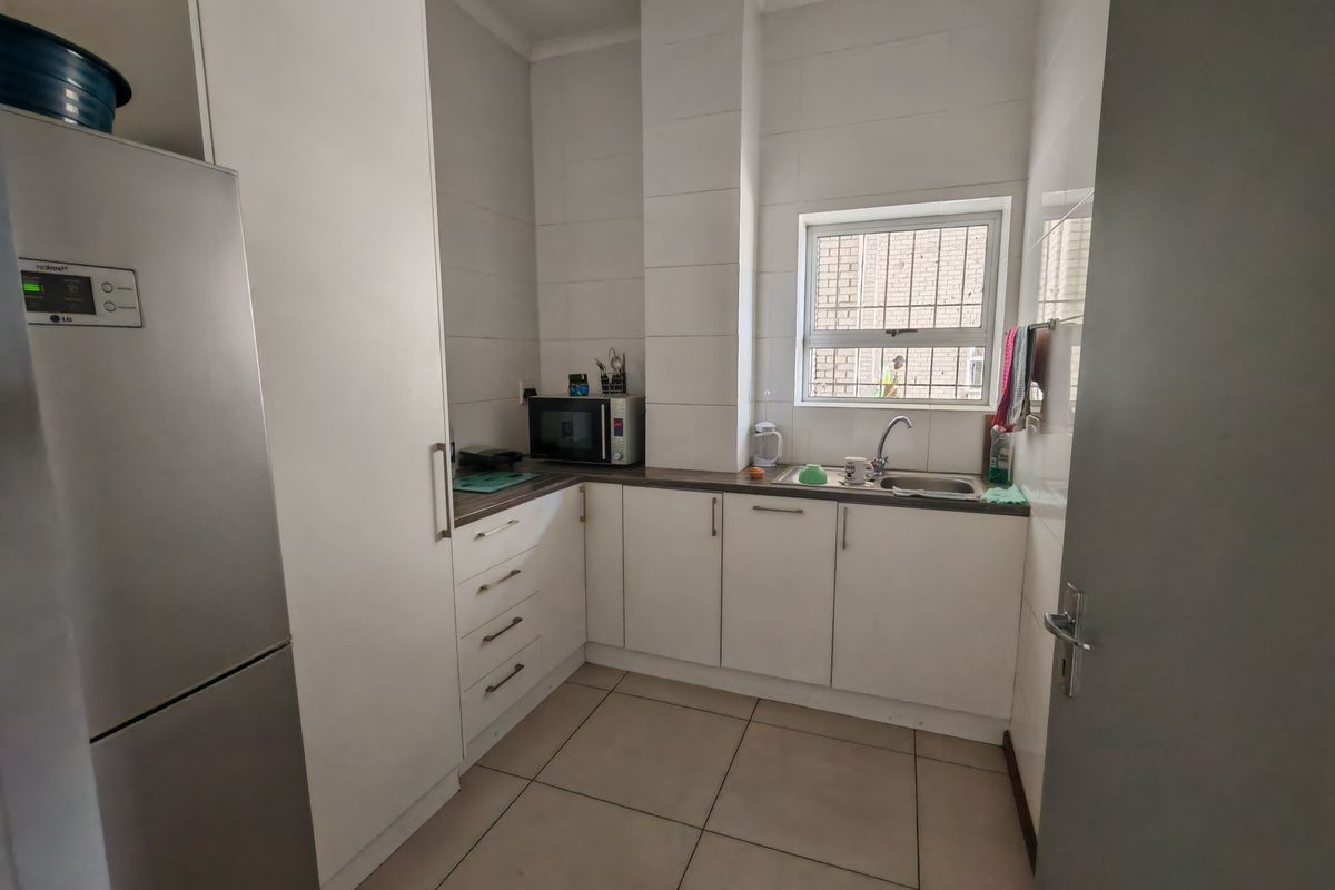 A compact kitchen featuring white cabinetry, tiled walls, tiled flooring, and a stainless steel sink with a window view.