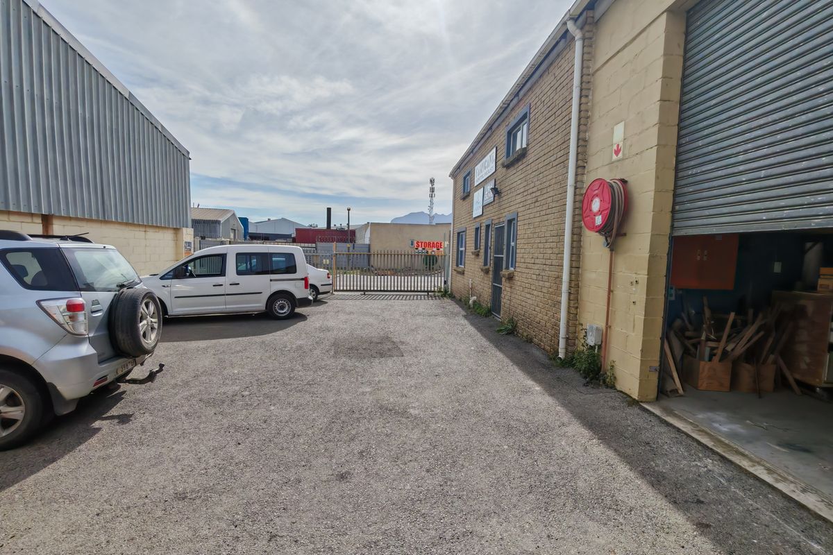 Industrial exterior yard area featuring a roller shutter door, brick facade, and fire hose reel, providing functional access and parking space.