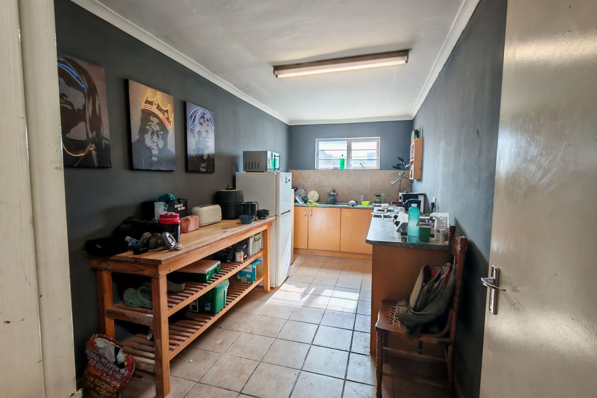 A functional kitchen area featuring wooden cabinetry, tiled flooring, and a stainless steel sink, providing a practical workspace for industrial or office use.