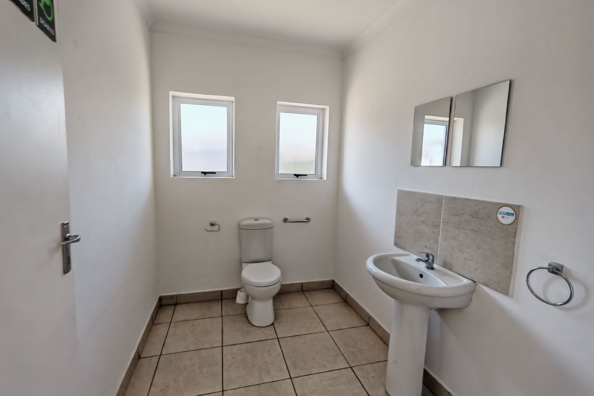A functional office restroom featuring a pedestal basin, toilet, tiled flooring, and wall-mounted mirrors.