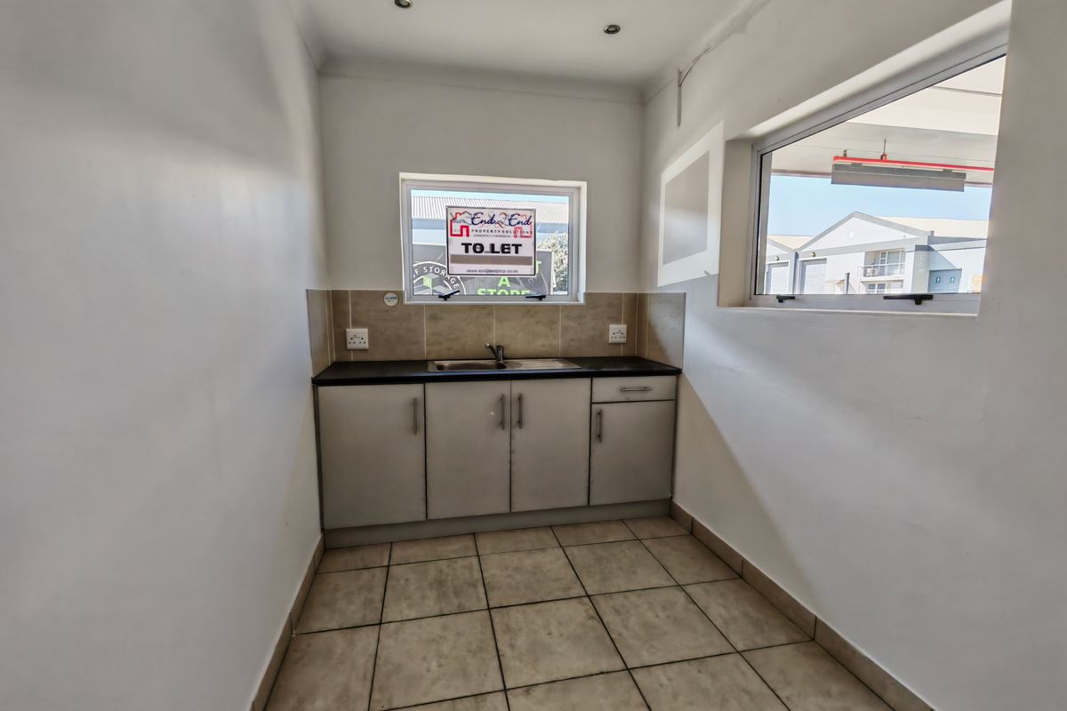 A functional kitchenette area featuring built-in cabinetry, a stainless steel sink, tiled splashback, and tiled flooring within an office space.