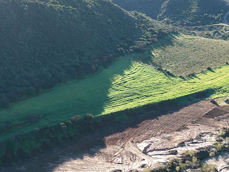 An aerial view of the small holding property, showcasing expansive green fields, natural hillside vegetation, and cleared earth sections.