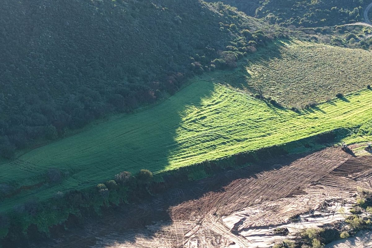 An aerial view of the small holding property, showcasing expansive green fields, natural hillside vegetation, and cleared earth sections.
