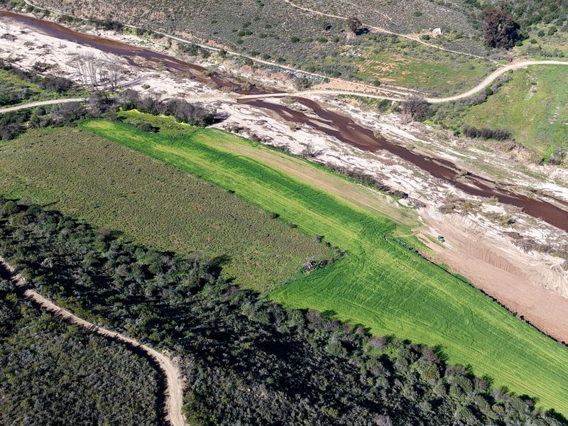Aerial view of the small holding property featuring a river, cultivated agricultural land, and natural vegetation with access via a dirt road.