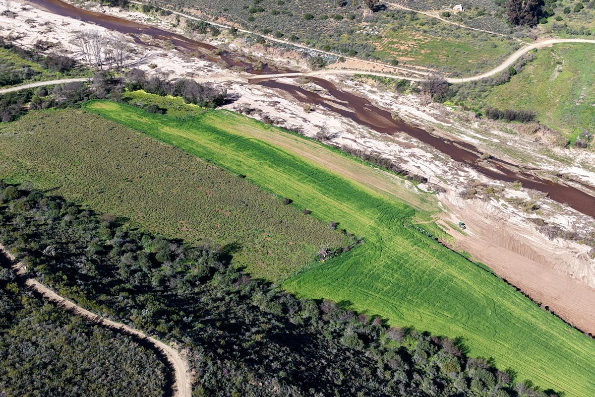 Aerial view of the small holding property featuring a river, cultivated agricultural land, and natural vegetation with access via a dirt road.