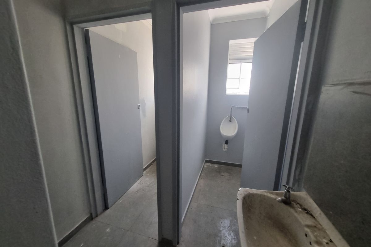 Industrial restroom facility featuring a wall-mounted urinal, tiled flooring, and a washbasin, requiring maintenance and cosmetic updates.