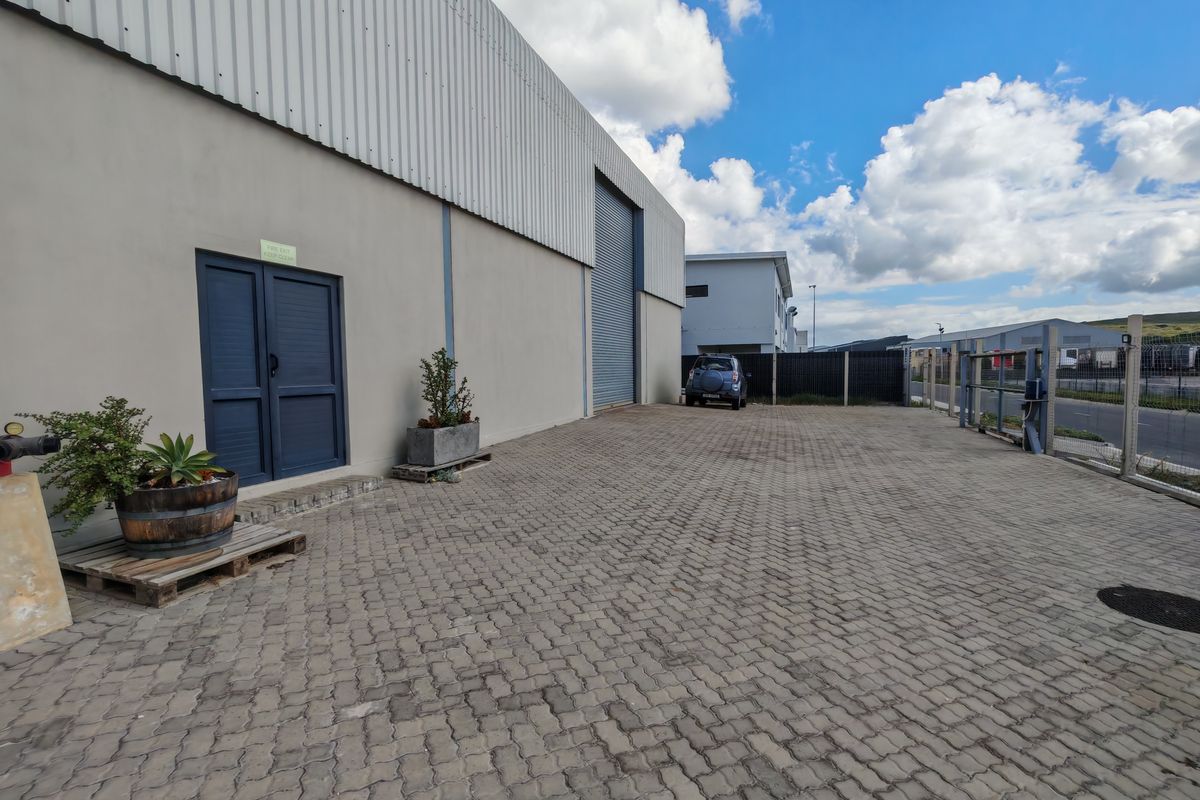 Exterior view of an industrial warehouse facility featuring a paved yard, roller shutter door, and secure perimeter fencing.
