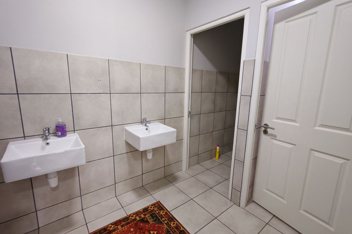 A functional washroom area featuring dual wall-mounted ceramic basins, tiled walls, and tiled flooring, providing a clean and practical utility space.