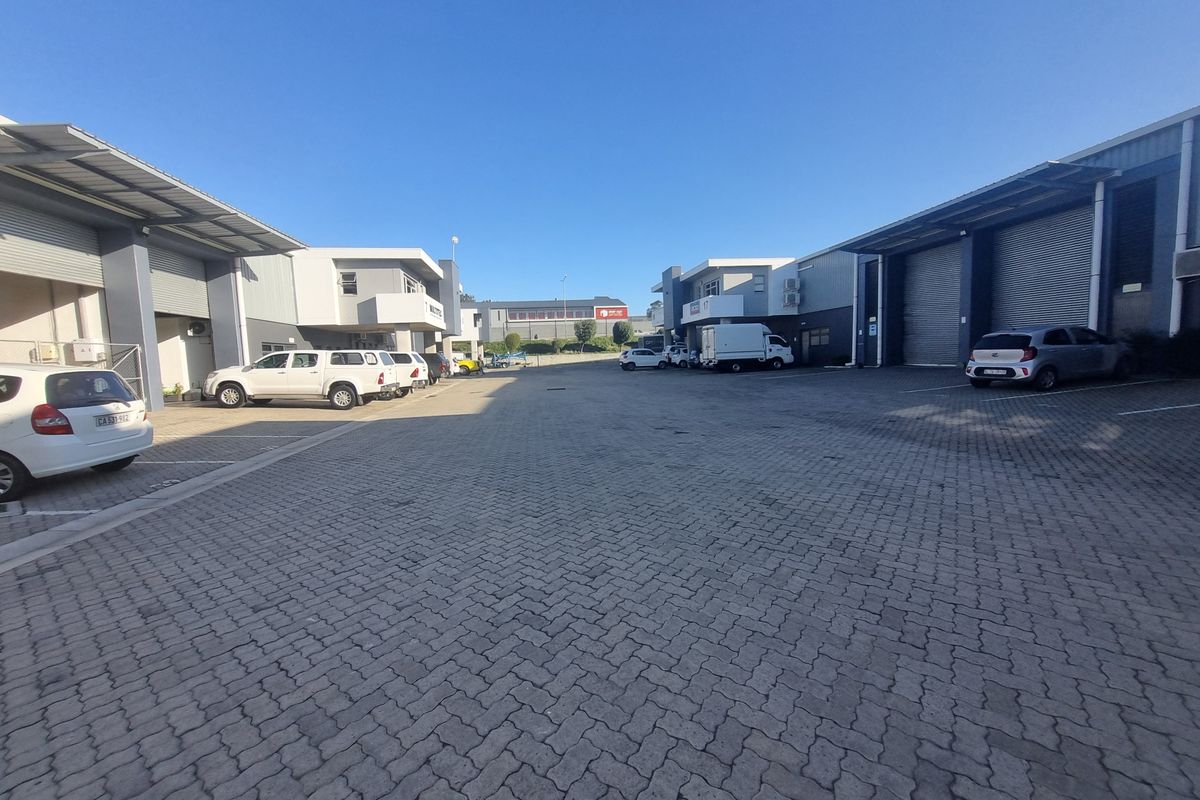 Exterior view of an industrial business park featuring paved parking area and multiple warehouse units with roller shutter doors.