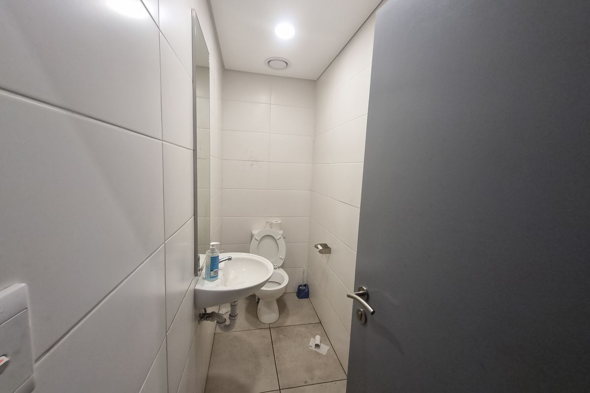A compact industrial-style restroom featuring white wall tiles, a wall-mounted basin, and a standard toilet suite.
