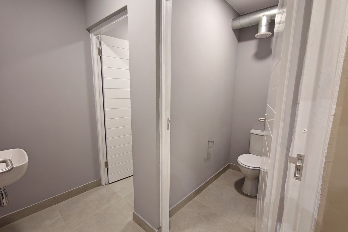 A clean, modern industrial-style restroom featuring a wall-mounted basin, a private toilet cubicle, and exposed ventilation ducting.