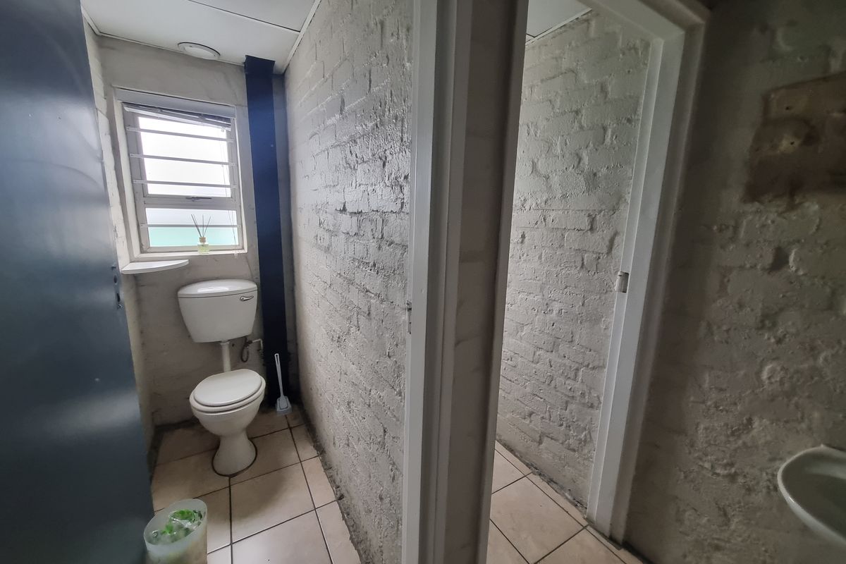 A basic office restroom featuring a toilet, tiled flooring, and exposed painted brick walls, requiring cosmetic updates and maintenance.