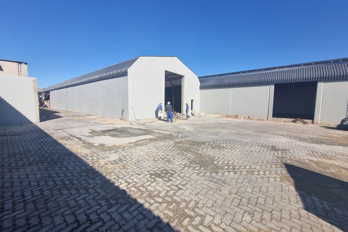 Exterior view of industrial warehouse buildings featuring large roller shutter access points and paved yard area under construction.