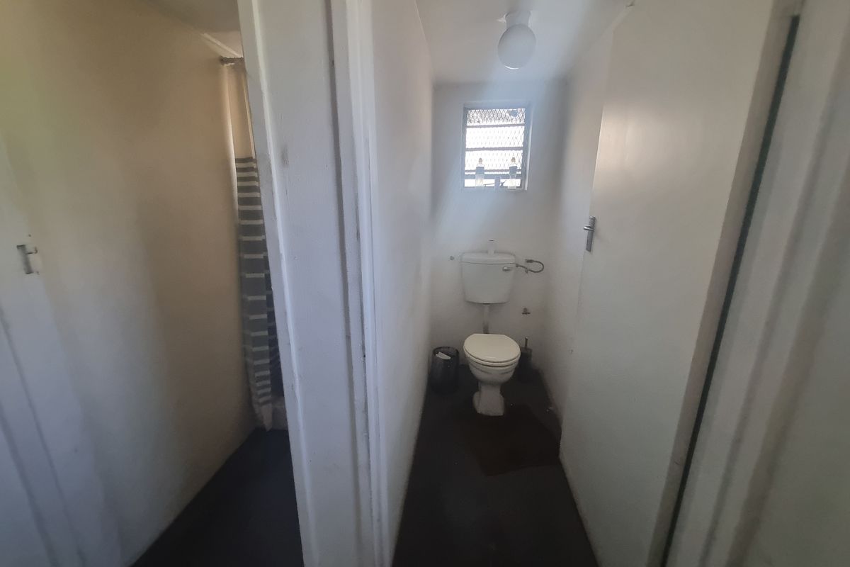 A functional bathroom featuring a standard toilet and a separate shower area with a curtain, reflecting a dated industrial-style utility space.