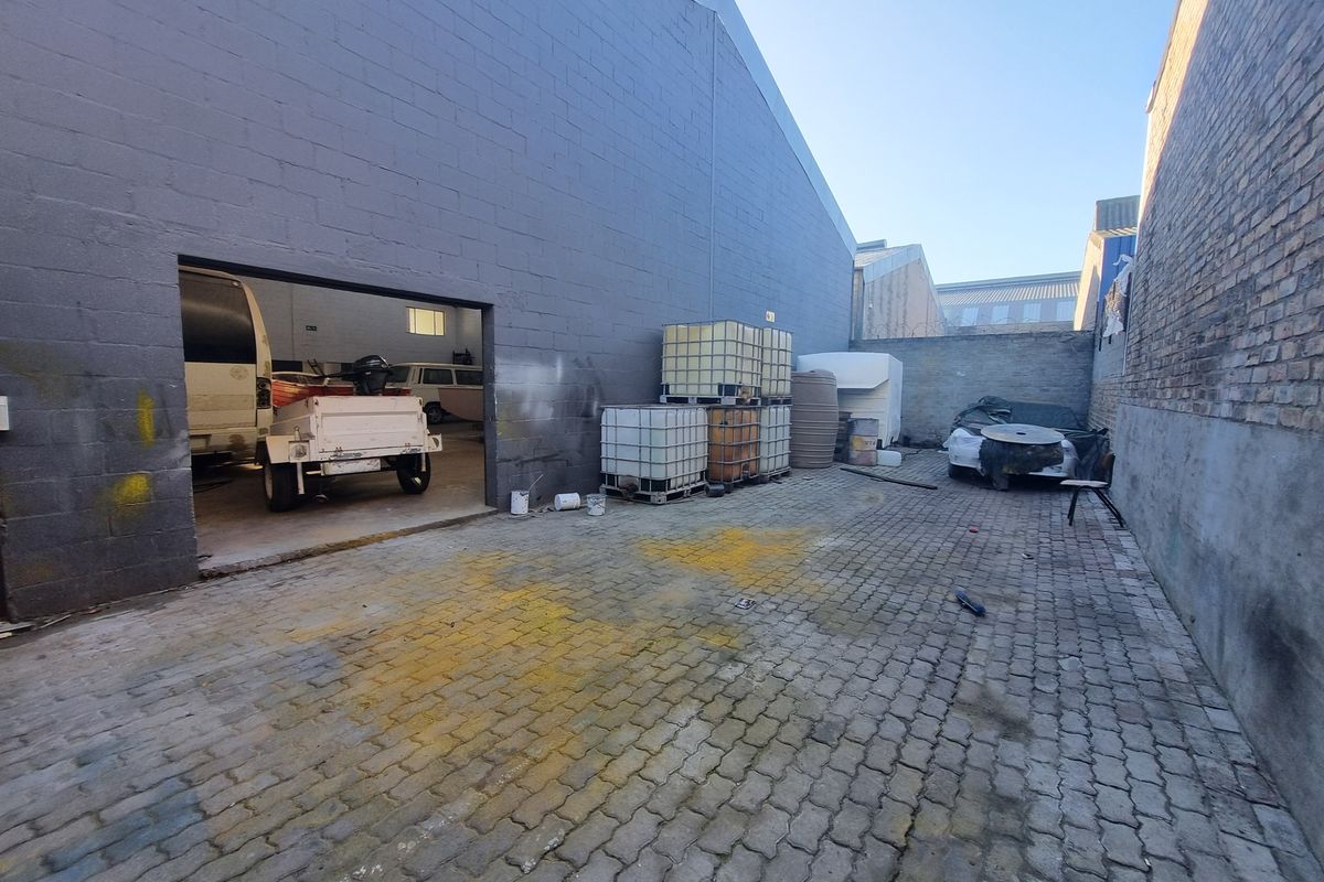 Industrial exterior yard space featuring paved ground, concrete block walls, and access to a large warehouse storage area.