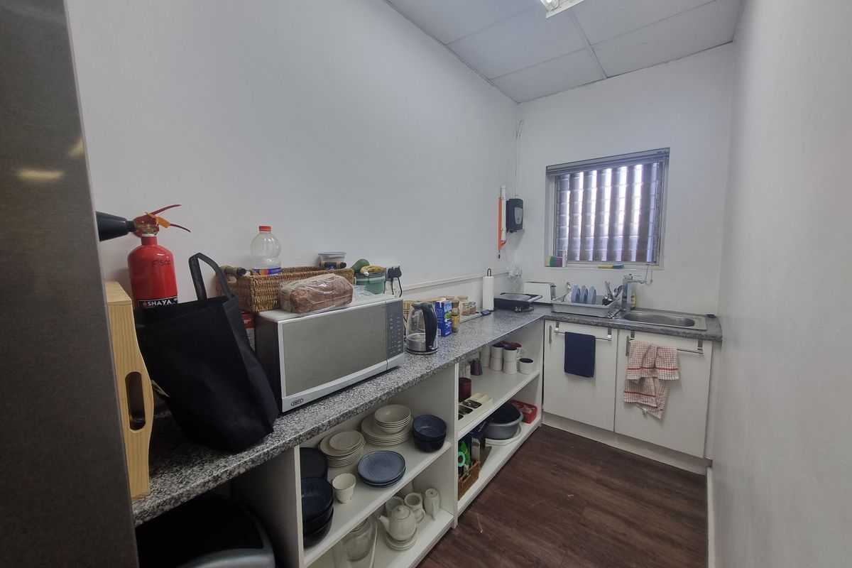 A functional kitchenette featuring granite-look countertops, open shelving, a stainless steel sink, and a window with vertical blinds.