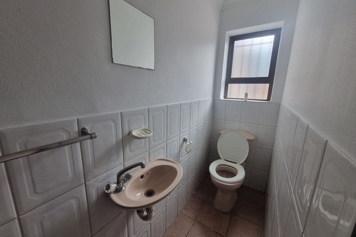 A functional guest bathroom featuring a wall-mounted basin, toilet, and tiled wall finishes with a window for natural ventilation.