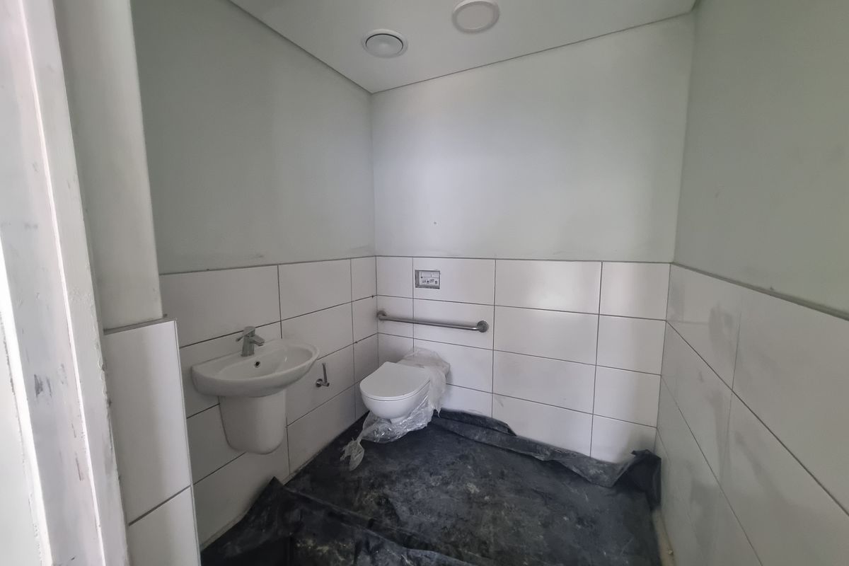 A functional, newly installed bathroom featuring white wall tiling, a wall-mounted basin, and a toilet with a grab rail.