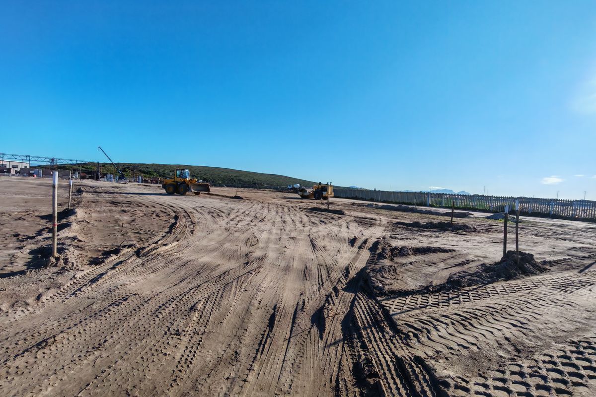 Expansive industrial development site featuring cleared, leveled earth with ongoing site preparation and perimeter fencing.