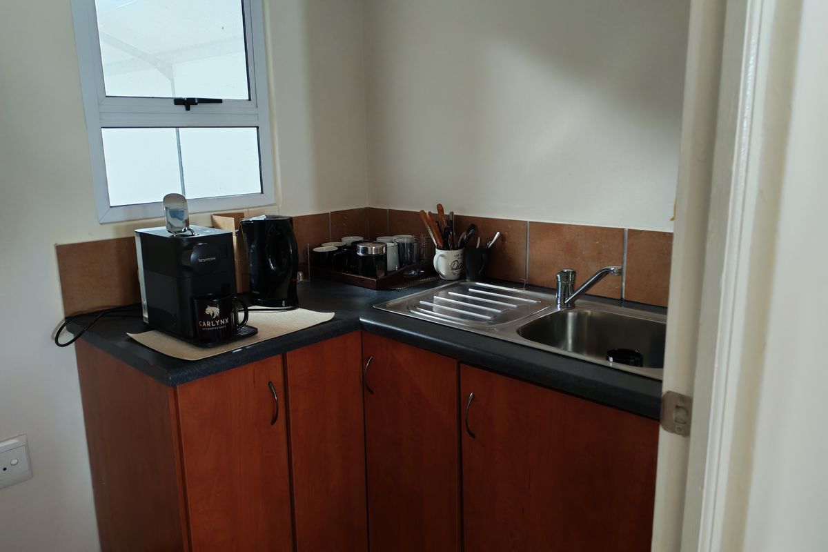 A compact kitchenette area featuring wooden cabinetry, a stainless steel sink with mixer tap, and tiled splashbacks.