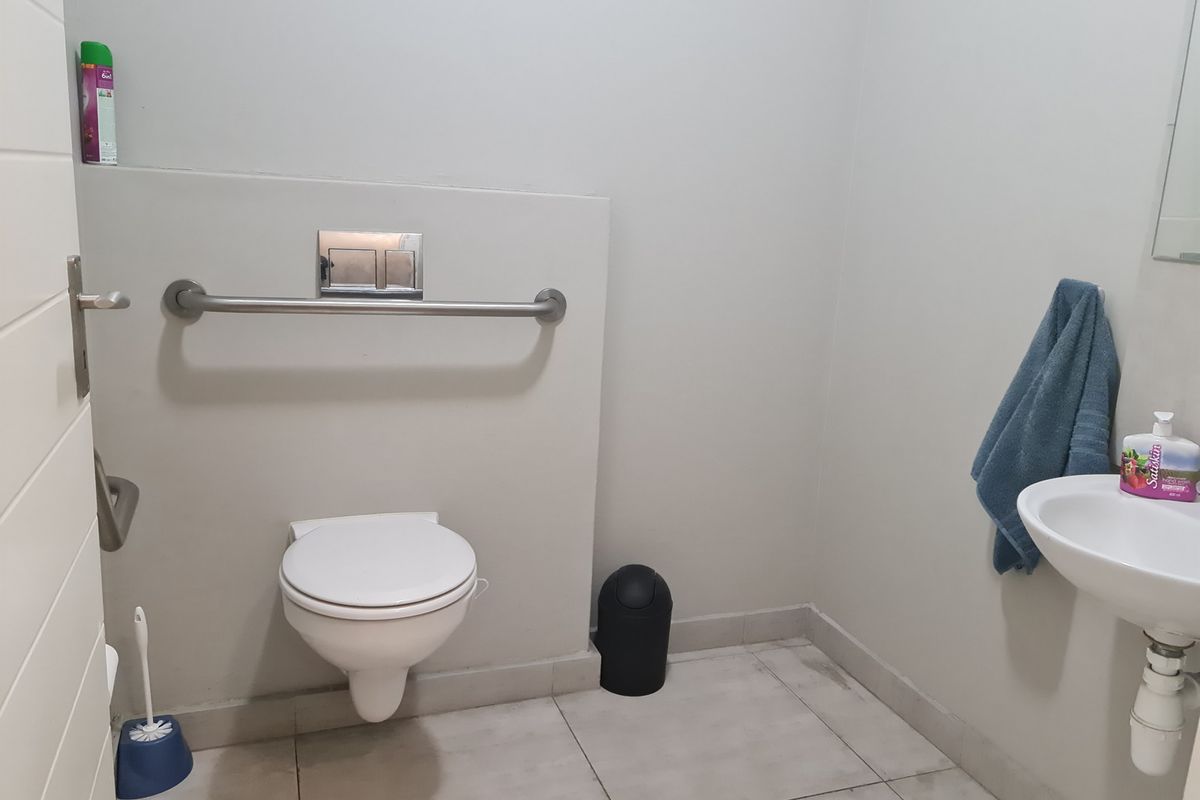 A functional accessible restroom featuring a wall-mounted toilet, grab rail, and a small wall-mounted basin.