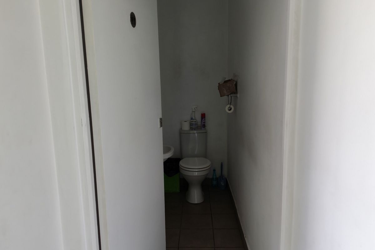 A compact industrial restroom featuring a standard toilet and wall-mounted basin with tiled flooring.