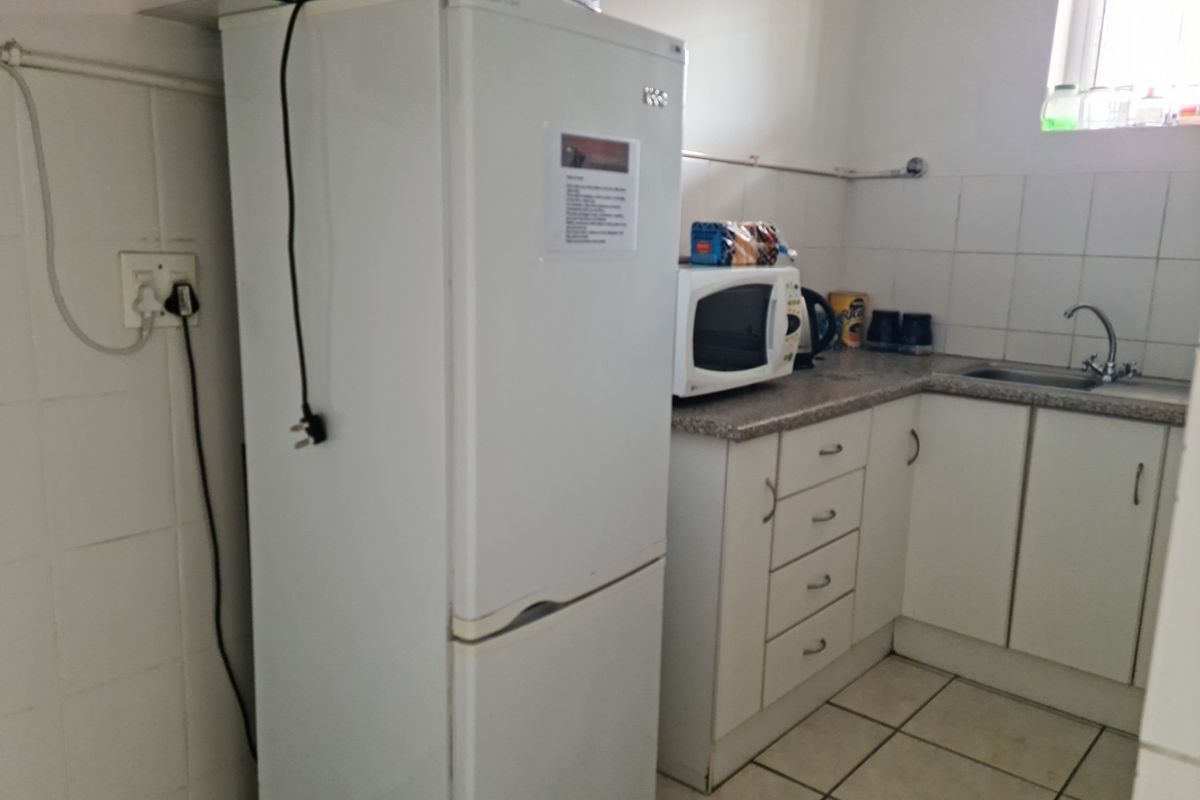 A functional kitchen area featuring white cabinetry, a stainless steel sink, tiled splashbacks, and tiled flooring in an industrial property setting.