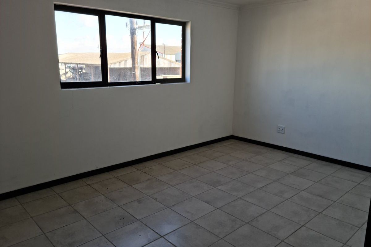 An empty, neutral-toned room featuring tiled flooring, a large window, and standard electrical outlets, suitable for use as an office or bedroom space.