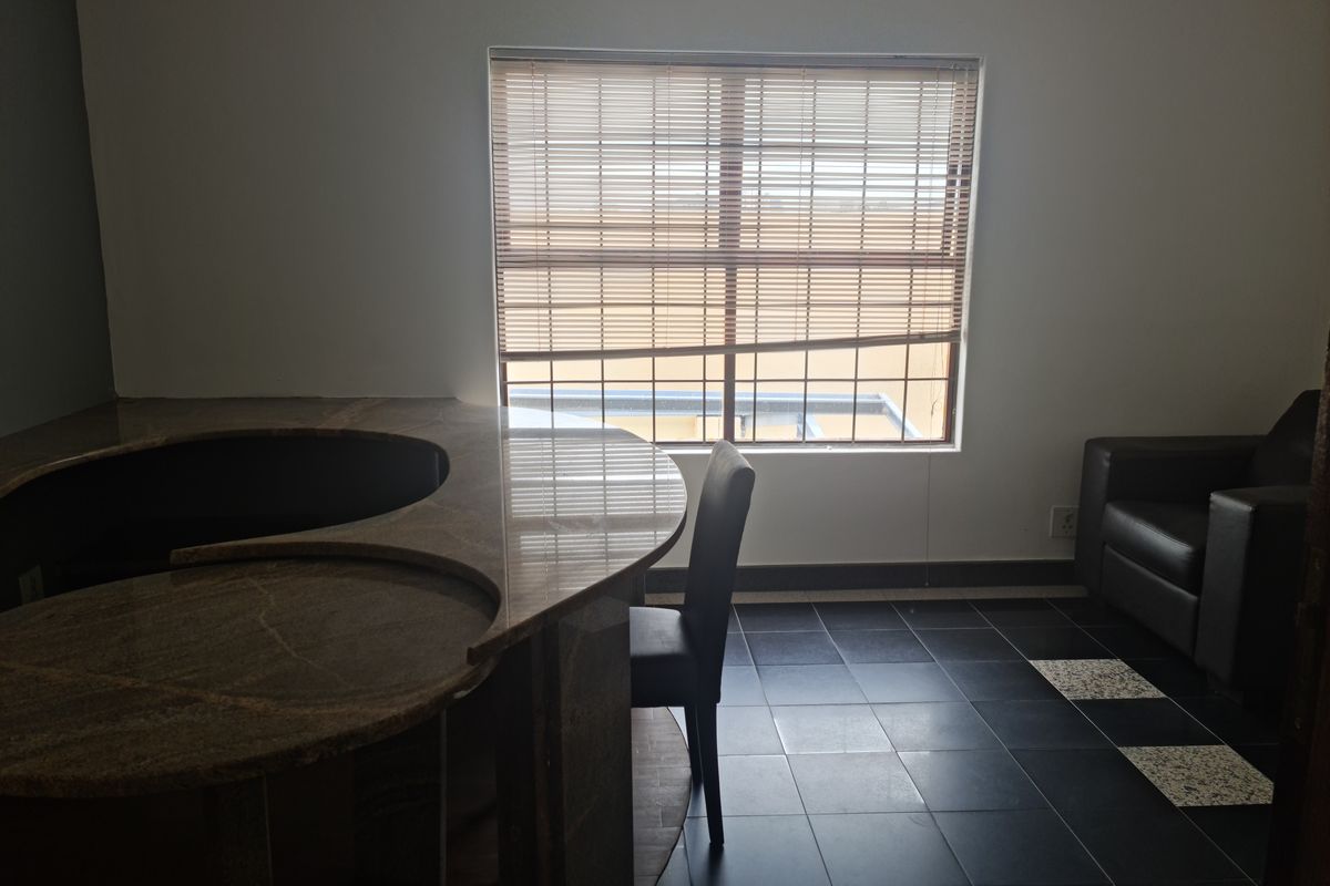 An interior view of a room featuring a curved granite-topped counter, dark tiled flooring, and a window with fitted blinds.