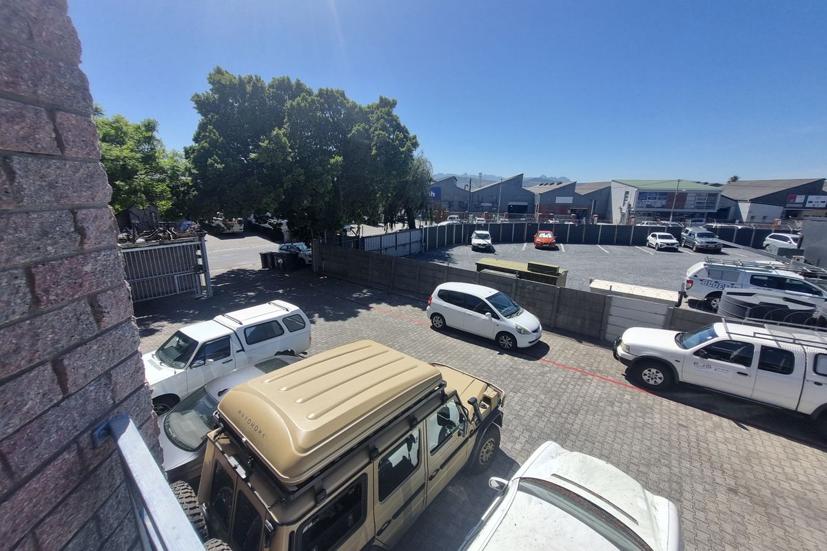 Elevated view of an industrial property parking area featuring paved surfaces, perimeter boundary walls, and access gates.