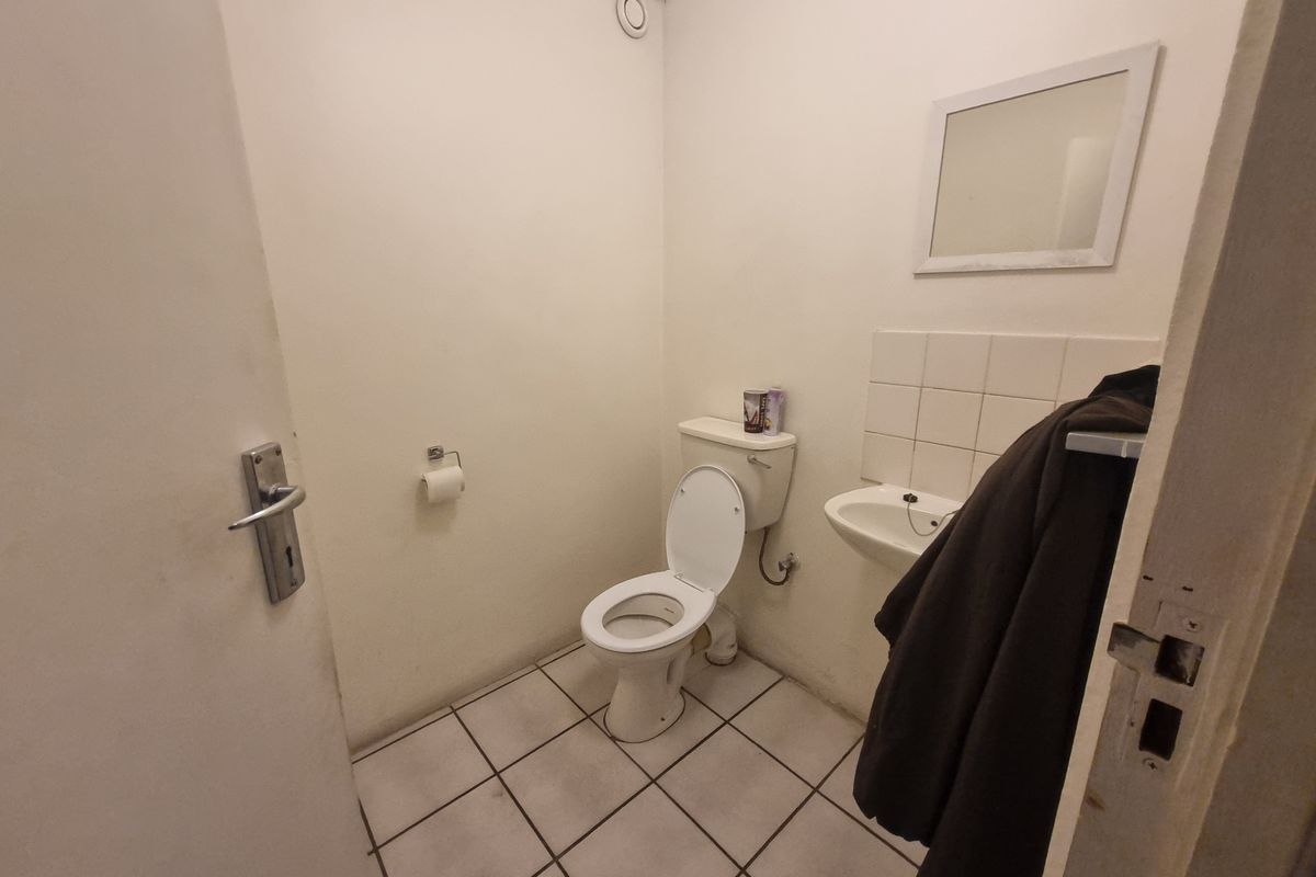 A functional industrial-style restroom featuring a standard toilet, wall-mounted basin with tiled splashback, and tiled flooring.