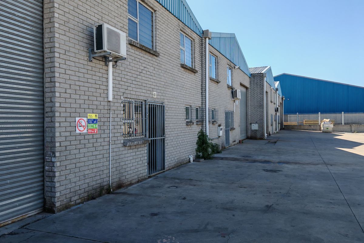 Exterior view of an industrial warehouse complex featuring brick facade, roller shutter doors, and concrete yard space.
