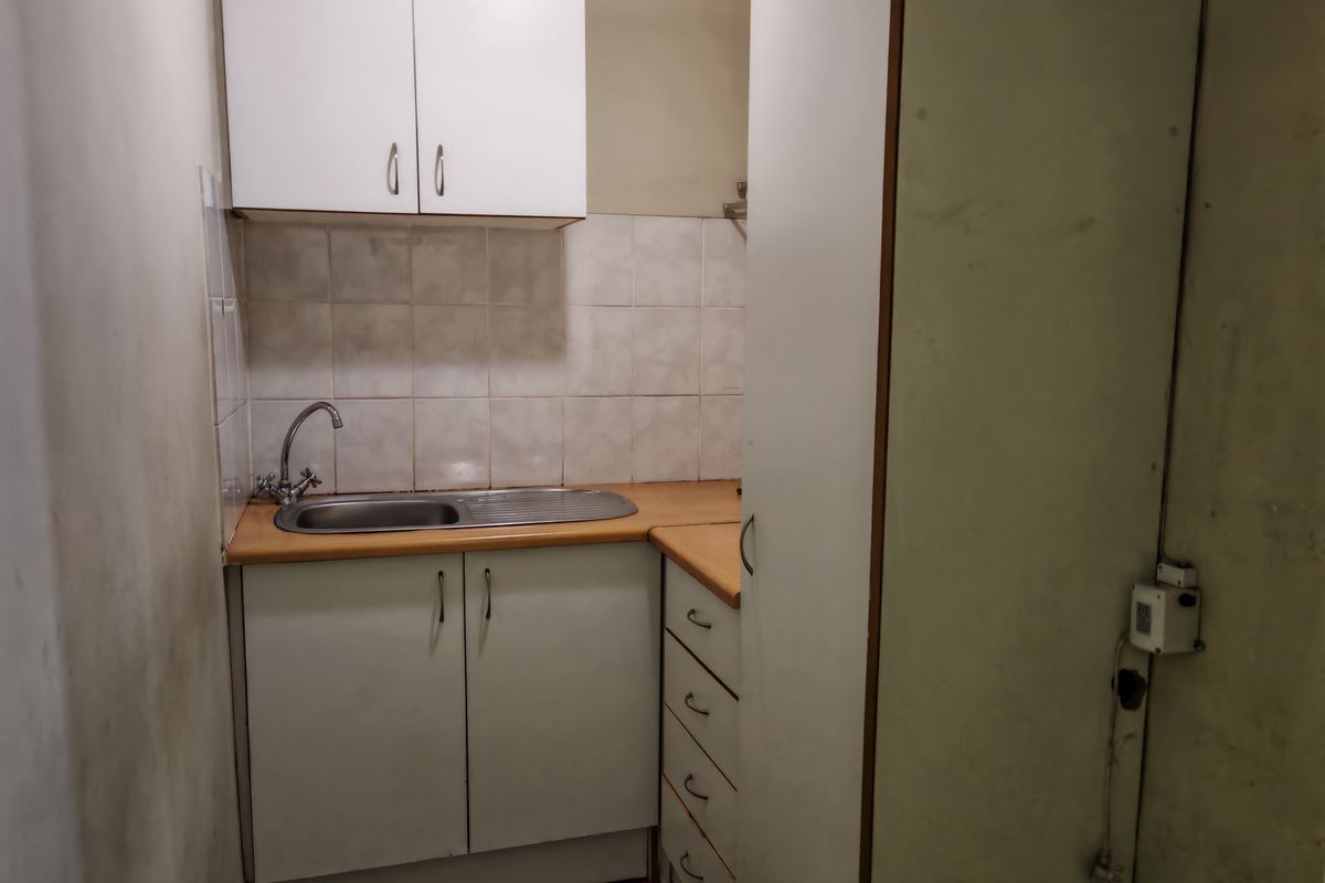 A compact kitchenette featuring built-in cabinetry, a stainless steel sink, and tiled splashbacks, suitable for a small industrial office or utility space.