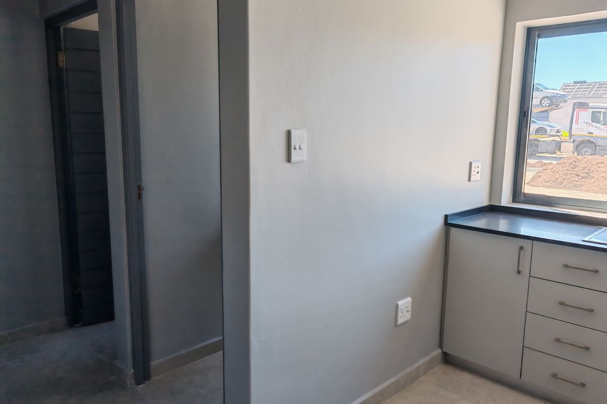 A clean, modern interior space featuring grey cabinetry, a dark countertop, and neutral tiled flooring with access to adjacent rooms.