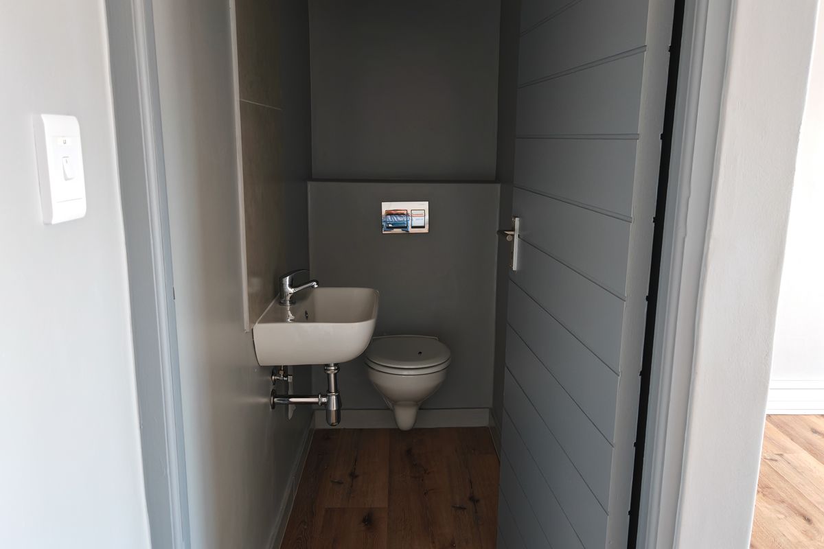 A modern, compact guest bathroom featuring a wall-mounted toilet with a chrome flush plate and a small wall-hung basin with wood-look flooring.
