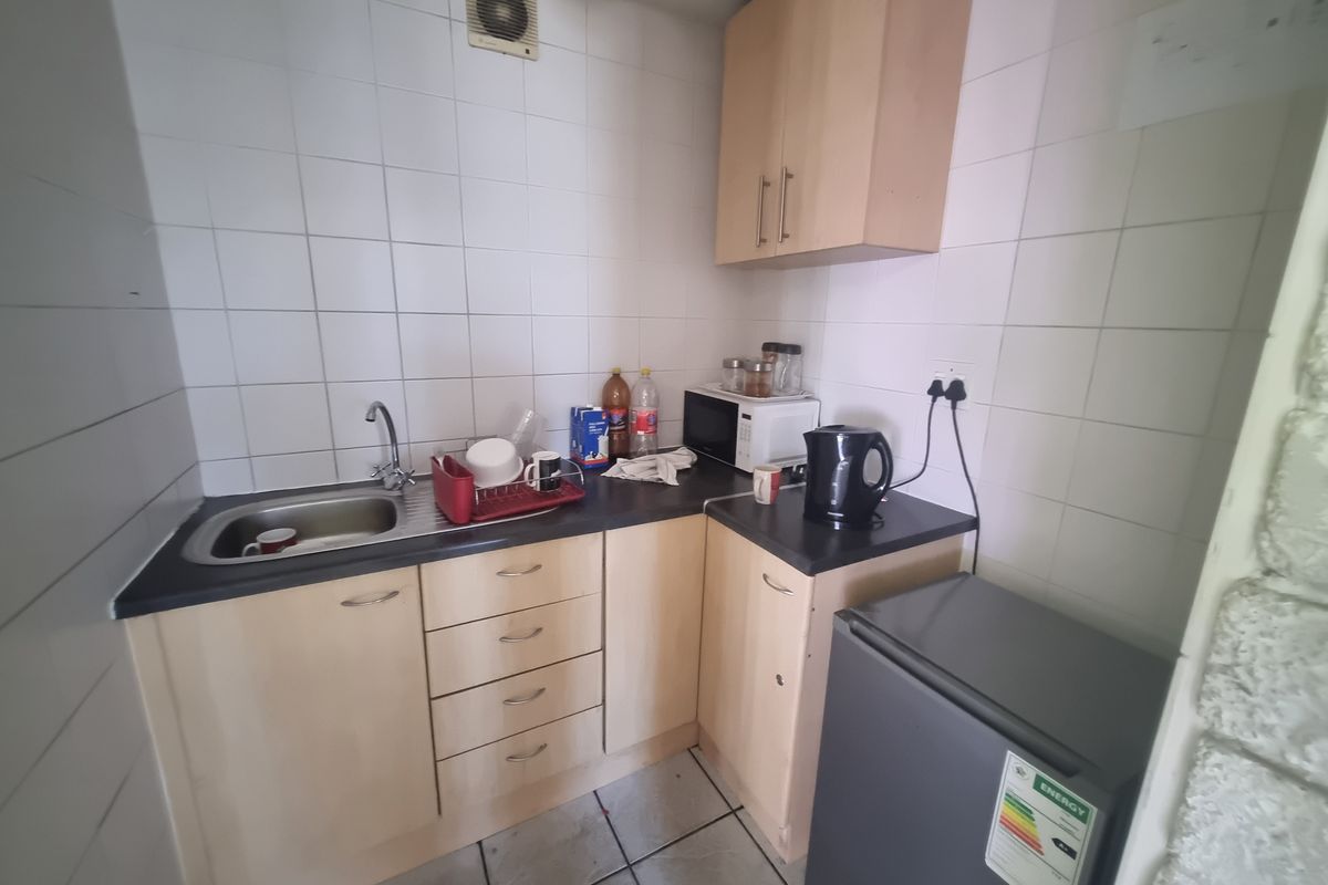 Compact kitchenette featuring light wood cabinetry, dark laminate countertops, stainless steel sink, and integrated extractor fan with tiled splashback.