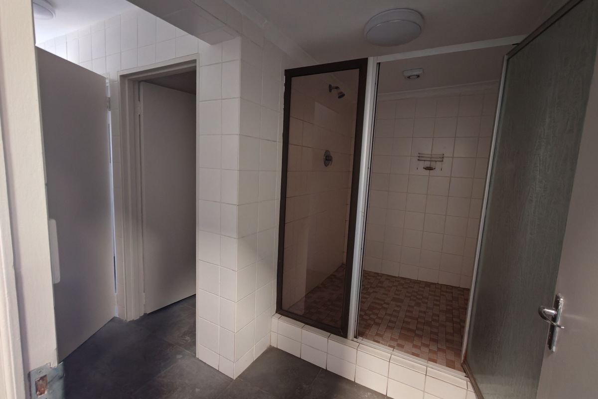 A functional bathroom featuring a walk-in shower with tiled walls and flooring, adjacent to a hallway with access to additional rooms.