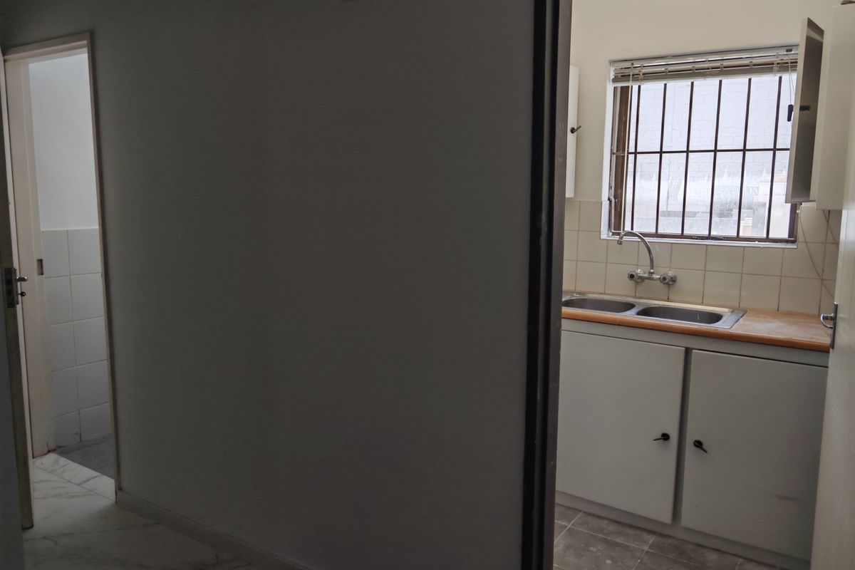 A functional kitchen area featuring a double basin sink, tiled splashback, and built-in cabinetry, with an adjacent tiled hallway.